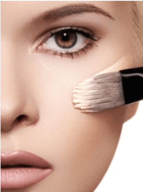 Makeup brush applying cream to a person's face with a close-up view.